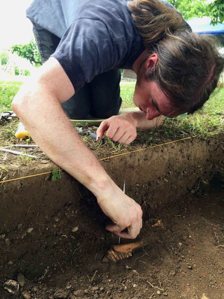 A male student digs in the dirt unearthing historical artifacts