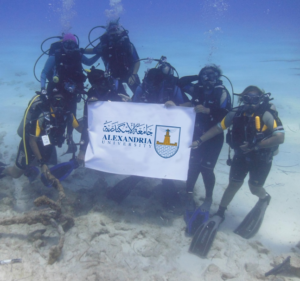 The Maritime Archaeology in Department of Archaeology and Greco-Roman Studies, Alexandria University group posing underwater while holding up the Alexandria University banner
