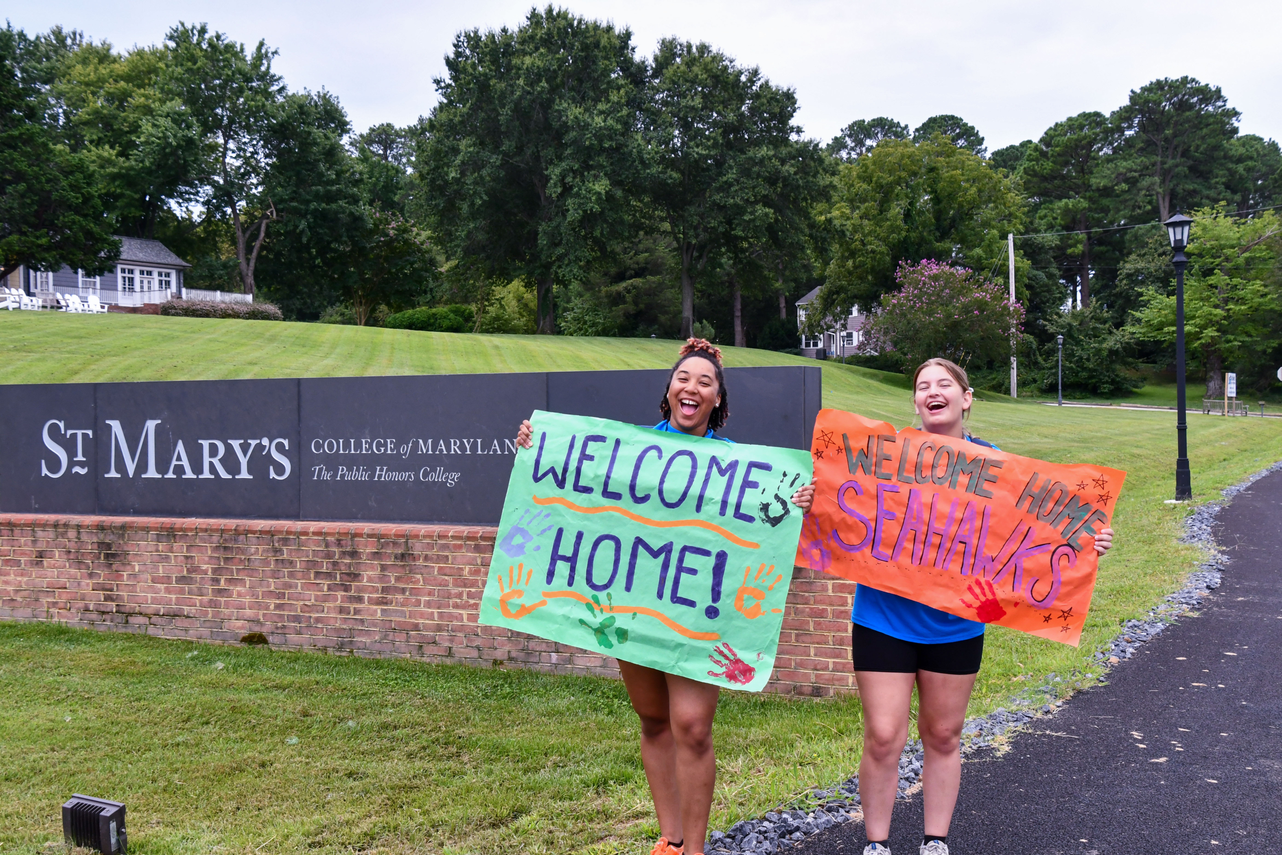 Two students holding welcome home signs greeting the incoming freshmen on campus.