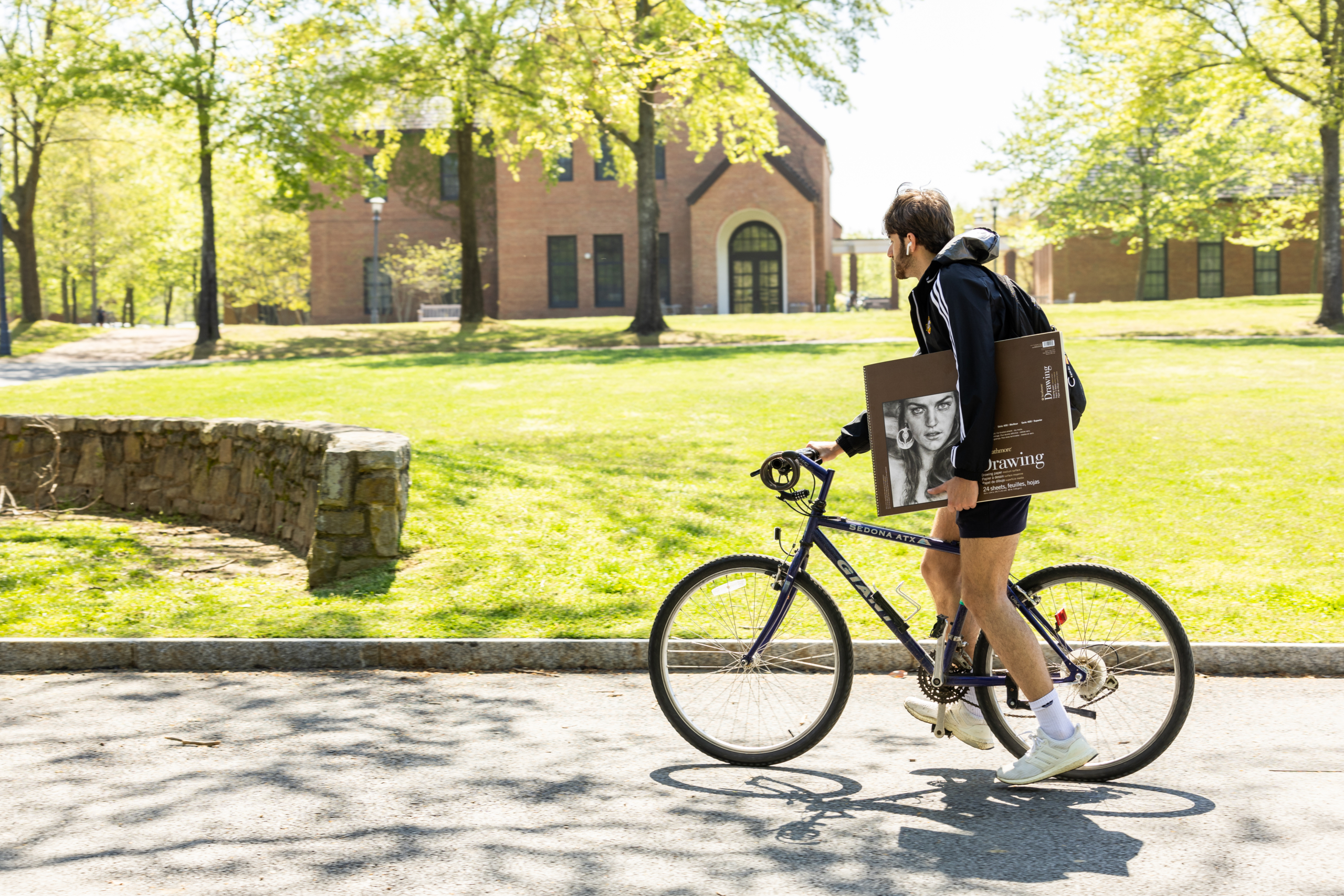 A SMCM student traveling to a new part of campus on a bike! While holding art supplies.