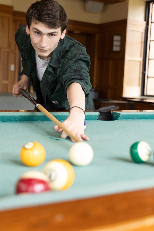 A student enjoying his free time playing pool in the commuter lounge.