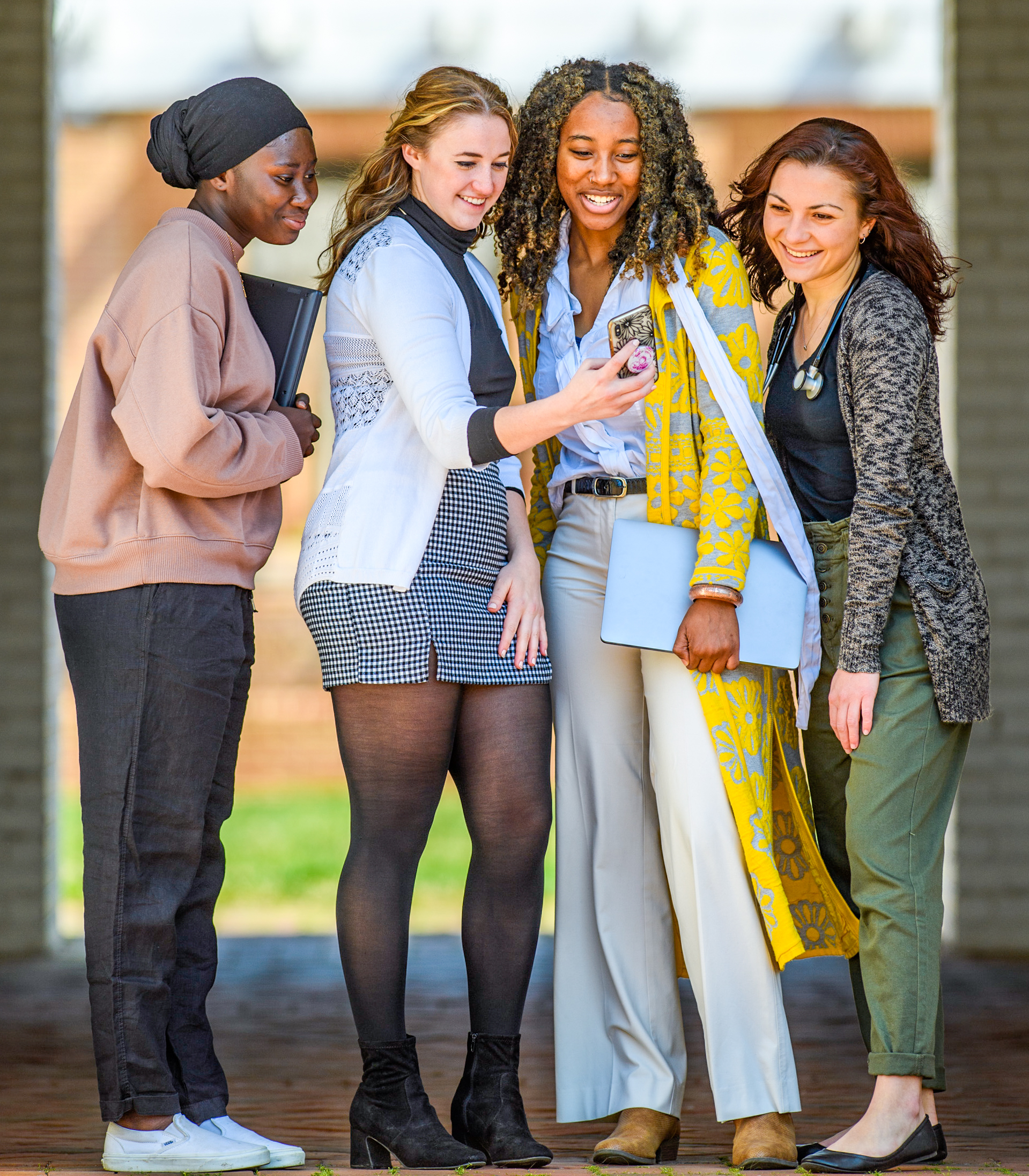 Photo of four smiling students on the campus of St. Mary's College of Maryland looking at an internship posting on a mobile phone