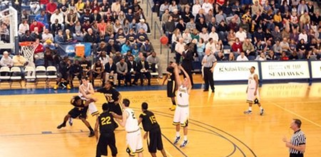 men in black and white uniforms play basketball on a court with people in the bleachers