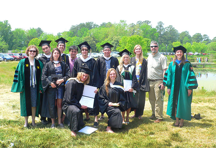 Thirteen students wearing cap and gown and holding their diplomas.