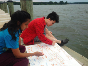 Two students work on their math project on a dock by the water