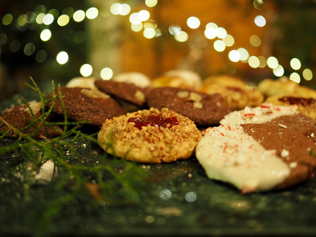 Maribeth Ganzell - Still life of holiday cookies on a platter of greenery with holiday lights background