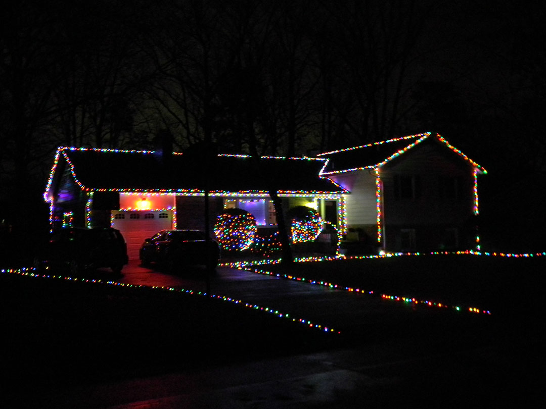 Aaron Koch - House decorated with colorful lights outlining the edges, hedges, and driveway