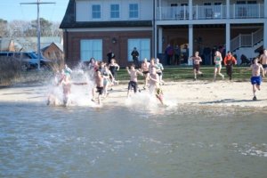 college students running into a river from a sandy beach