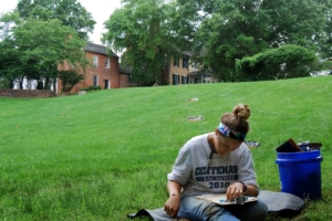 female student sitting outside on the grass reading a book