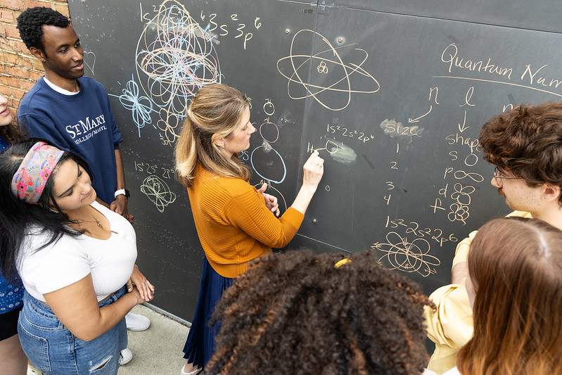 SMCM professor writing with chalk on a blackboard as students watch